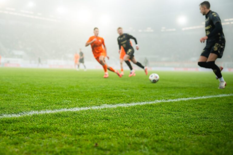 grass and sideline on the football pitch at the stadium and player's legs at the background